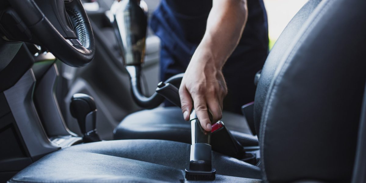 cropped view of car cleaner vacuuming drivers seat in car